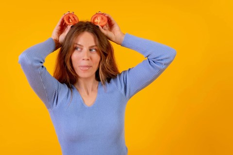 Vegan woman smiling with tomato slices on her head on a yellow background