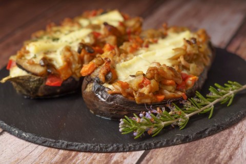 Foreground eggplant stuffed with meat and vegetables covered with bechamel sauce on a black slate on a wooden table