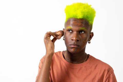 An androgynous black man posing putting on makeup