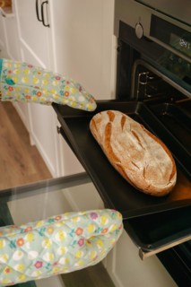 Loaf of bread in the oven tray with oven mitts
