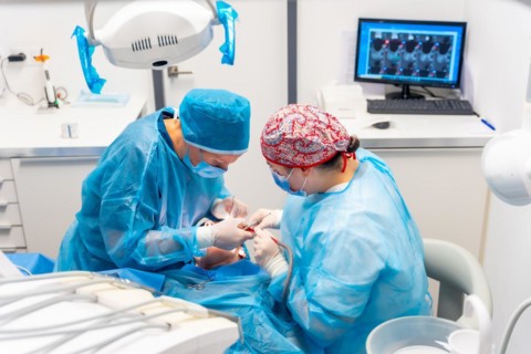 Female dentists in blue scrubs performing a complicated operation on a female patient