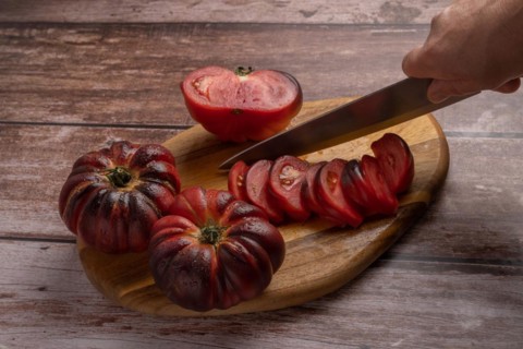 Close-up of a woman's hand with knife cutting tomatoes on a board on wooden table