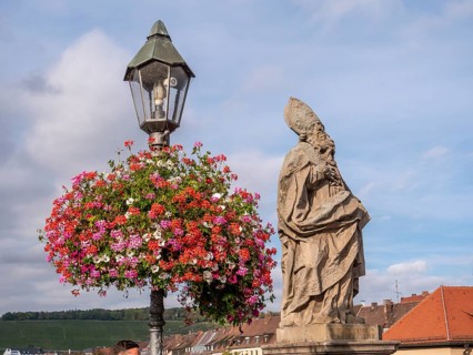 The flower-decorated streetlamp and the religious bridge statue of St. Fridericus on Alte Mainbruecke