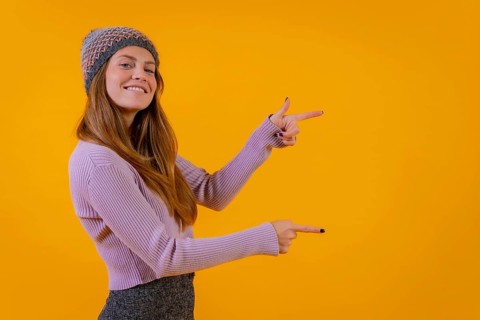 Woman with wool cap on a yellow background pointing to the right