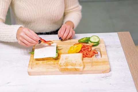 Unrecognizable person cooking a vegetable sandwich in the kitchen at home. Placing the red pepper