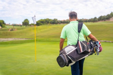 Portrait of male golfer walking down fairway carrying bags