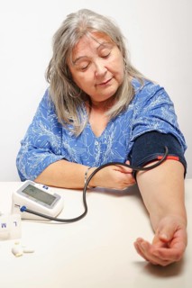 Older white-haired woman with glasses taking her blood pressure at home with white background
