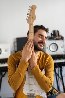Young boy with beard playing guitar at home with piano on the back