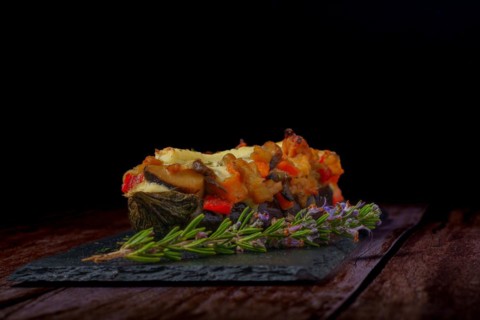 Eggplants stuffed with meat and vegetables with rosemary branch in flower and tomato cut on a black background