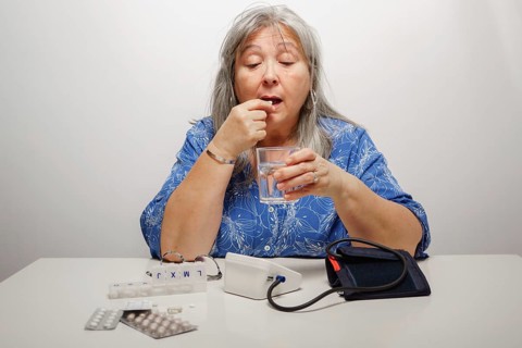 Older white-haired woman taking a pill after having her blood pressure checked