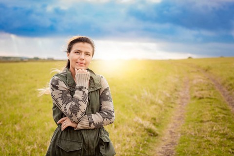 A woman on a path in the countryside sunset. Portrait of young woman with hand on chin on a beautiful country road. Smiling woman with hand on chin on a beautiful country road