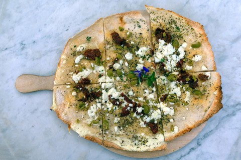 Flammkuchen with olives dried tomatoes and feta cheese on a wooden board
