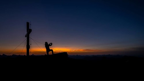 Mobile phone photographer at the summit cross of the Namloser Wetterspitze at sunset with Lechtaler Alpen