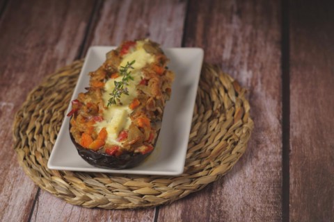 Eggplants stuffed with meat and vegetables on a white plate on a wooden table with a branch of rosemary in bloom