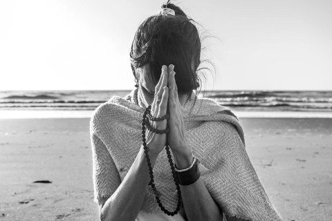 Portrait of a woman clasping hands while holding a japa mala at the beach. Namaste pose