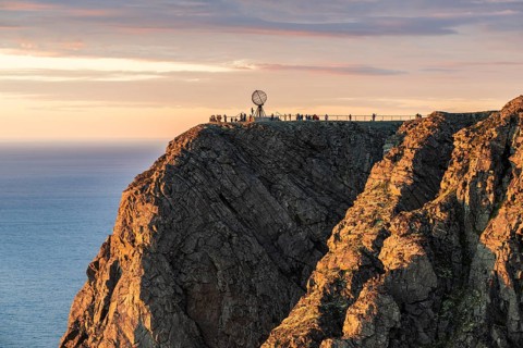 Rock cliff of the North Cape with steel globe at midnight sun
