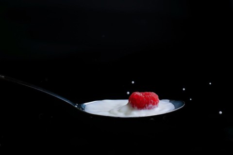 Raspberry splashing milk on a metal spoon splash effect with black background