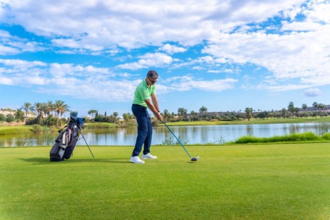 Male golf player on professional golf course. Golfer hitting the ball with driver stick next to a lake