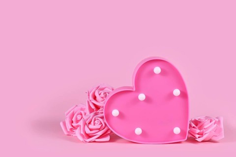 Valentine's day composition with roses and heart shaped lamp on pink background with copy space