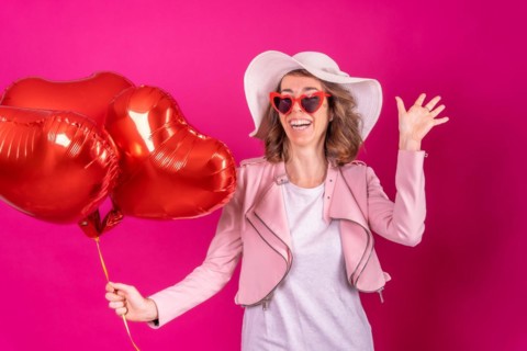 Portrait of a caucasian woman having fun dancing with a white hat in a nightclub with some heart balloons
