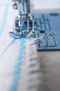 Close-up of sewing machine needle with blue thread sewing on a white fabric