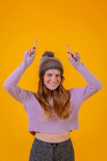 Woman with wool cap on a yellow background pointing up