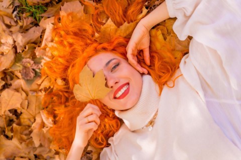 Red-haired woman lying on leaves in a park in a forest