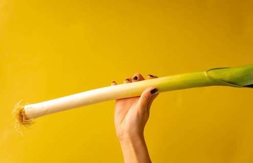 Woman's hand with a vegetable on a yellow background