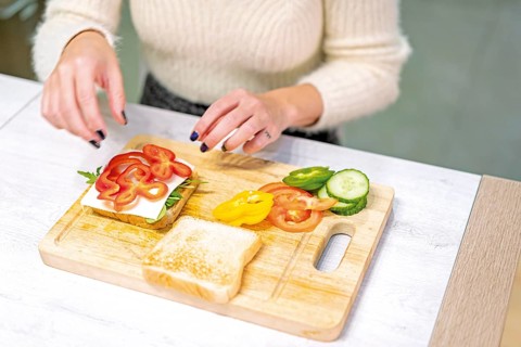 Unrecognizable person cooking a vegetable sandwich in the kitchen at home. Placing the red pepper