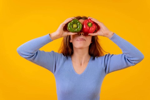 Vegetarian woman in a portrait with peppers in her eyes on a yellow background