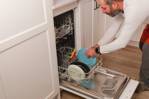 Man in white t-shirt putting the dishes in the dishwasher