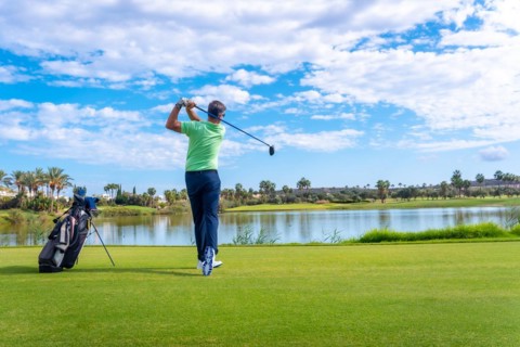 Man playing golf at golf club by a lake