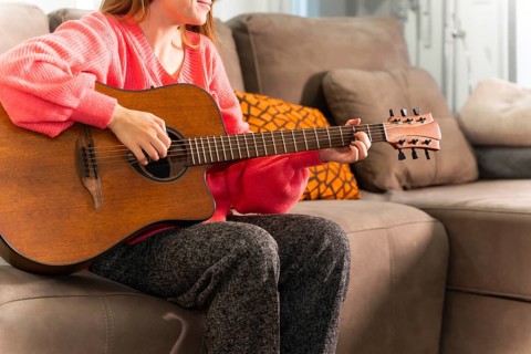Playing the guitar at home sitting on the sofa in her living room next to the sale