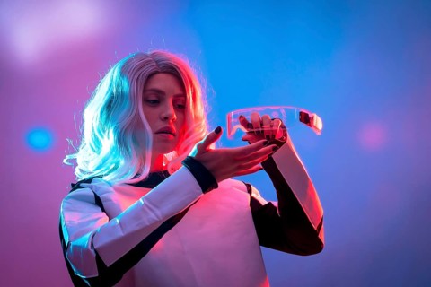 Beautiful woman adjusting futuristic glasses on a dark background