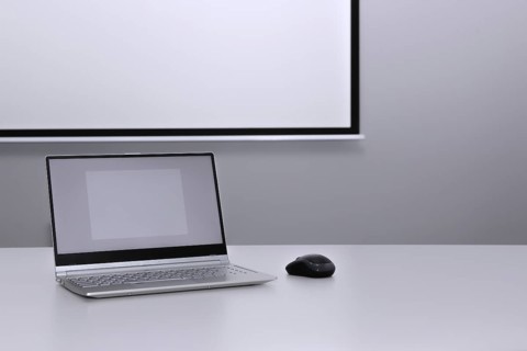 An unfolded laptop stands on a desk in front of a presentation screen