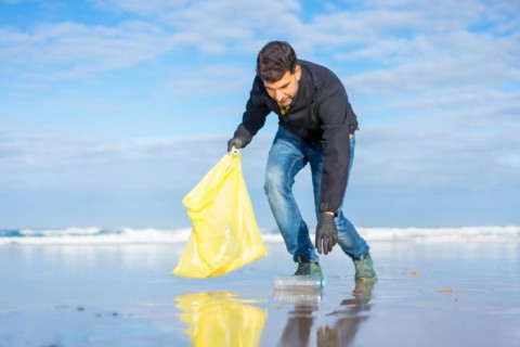 Volunteer man collecting garbage or plastic on the beach. Ecology concept