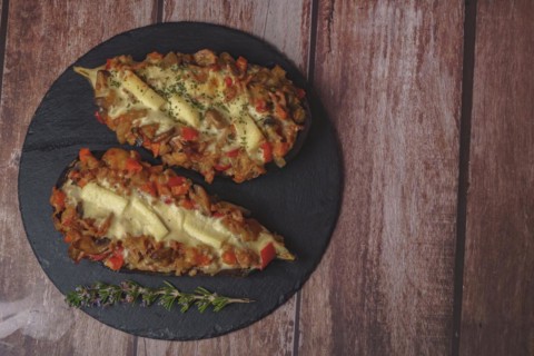 Foreground eggplant stuffed with meat and vegetables covered with bechamel sauce on a black slate on a wooden table