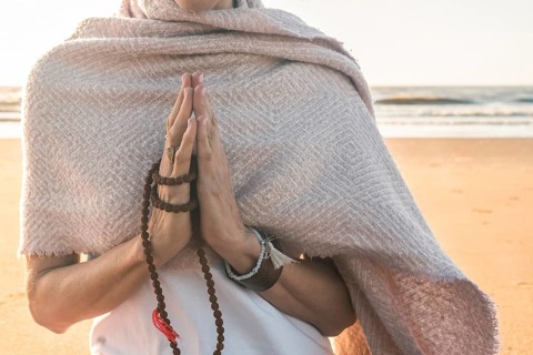 Close up of a woman clasping hands while holding a japa mala outdoors. Namaste pose