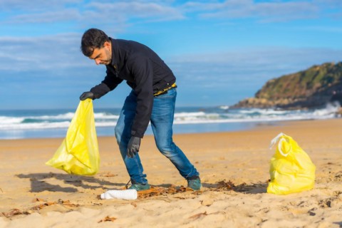 Volunteer person collecting plastic from the sand on the beach. Ecology concept