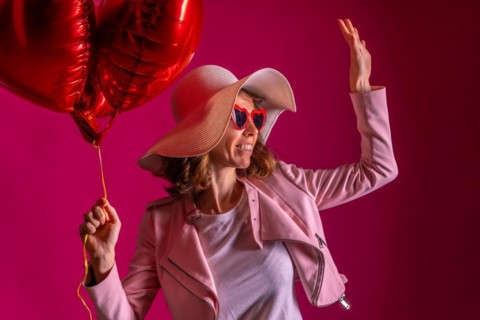 A caucasian woman with a white hat in a nightclub with some heart balloons