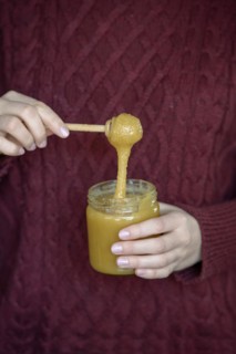 Hands holding honey jar with honey spoon
