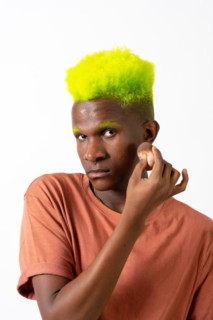 An androgynous black man posing putting on makeup