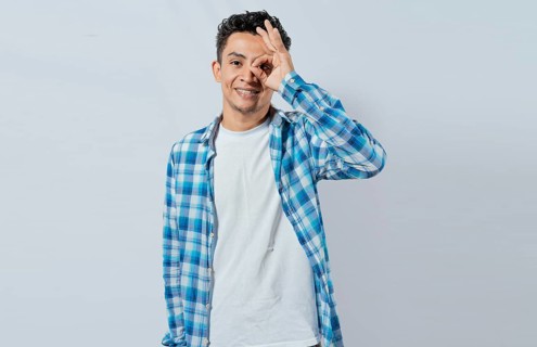 Happy young man making ok gesture with hand looking through fingers. Friendly man making ok gesture looking through fingers. Teenage guy making ok gesture looking through fingers