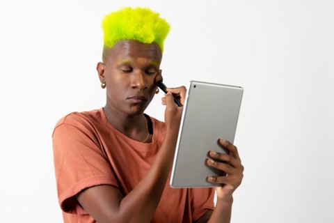 A gay black man putting on makeup