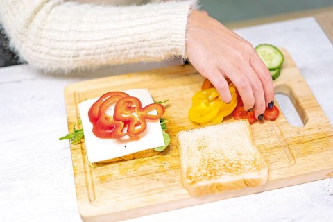 Unrecognizable person cooking a vegetable sandwich in the kitchen at home. Placing the red pepper