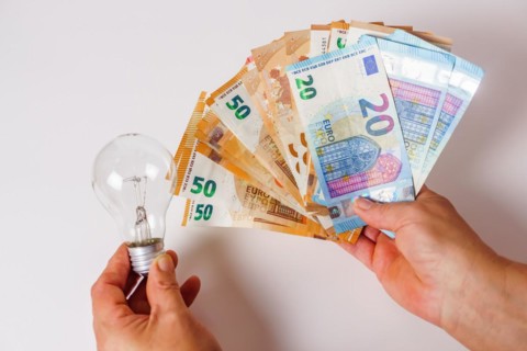 Woman holding banknotes in one hand and a light bulb in the other concept of light prices