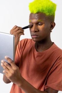 A gay black man putting on makeup