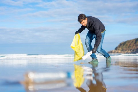 Volunteer man collecting garbage or plastic on the beach. Ecology concept