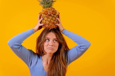 Woman with a pineapple in sunglasses in a studio on a yellow background
