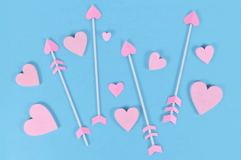 Pink Valentine's day cupid's arrows with heart shaped tips and heart ornaments on blue background
